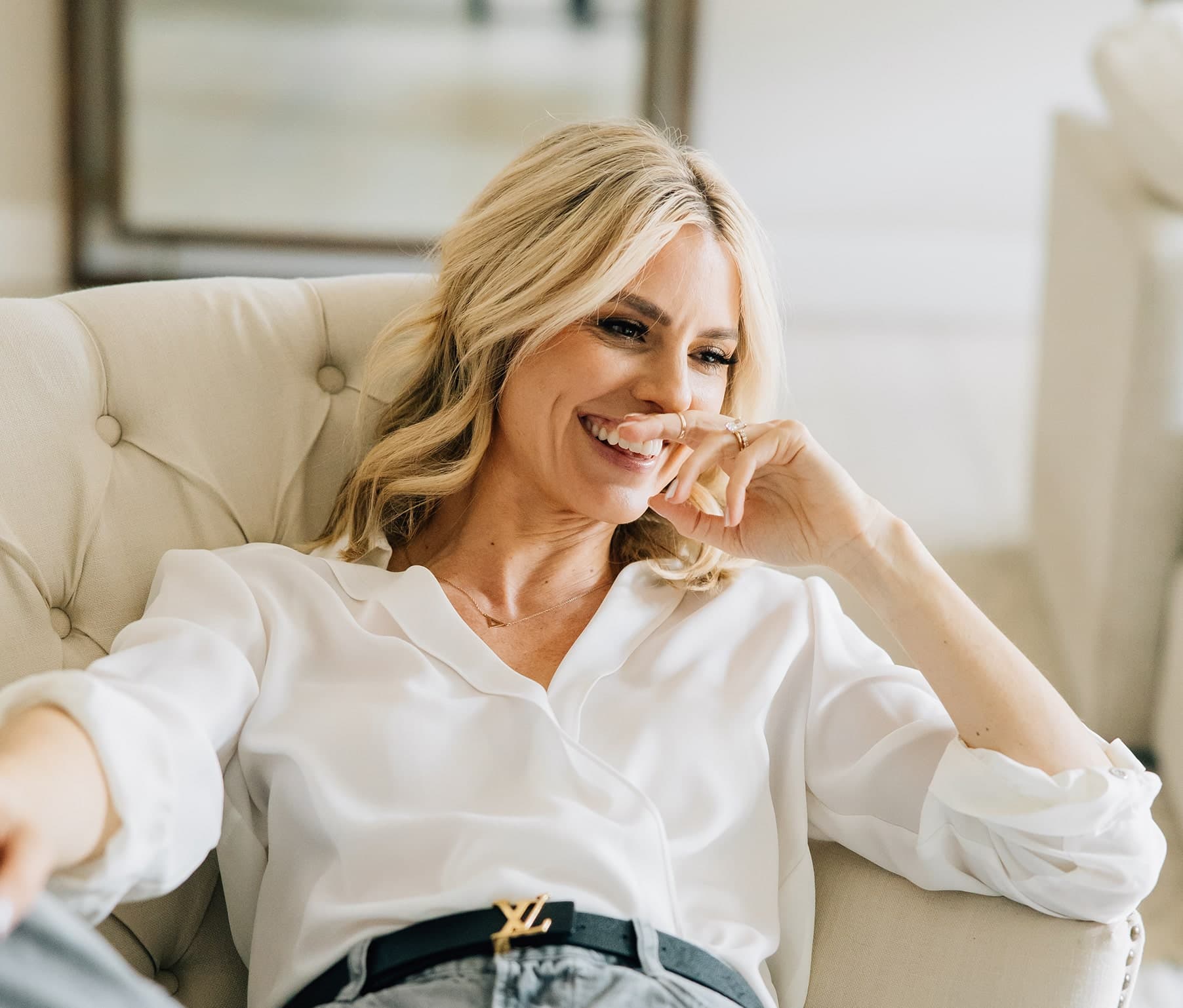 Keeli laughing in a chair with her hand near her mouth.